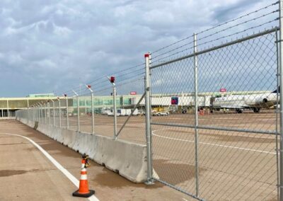AOA temporary fence panels with chain-link fencing, concrete barriers, and barbed wire, securing an aircraft operations area at an active airport.