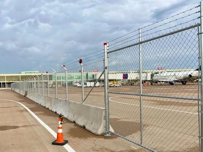 AOA Temporary Fence Panel Installation | Vector Fence AOA temporary fence panels with chain-link fencing, concrete barriers, and barbed wire, securing an aircraft operations area at an active airport.
