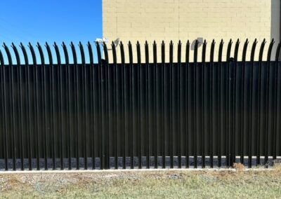 High-security commercial steel fence with curved anti-climb pickets installed around a protected facility.
