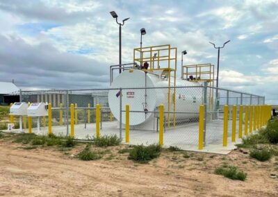 Commercial chain link security fence installation surrounding fuel storage equipment with safety bollards.