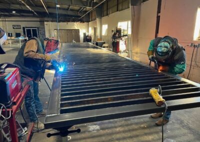Fabricators welding a custom steel gate in a fabrication shop, showcasing the custom residential and commercial gates built in-house.