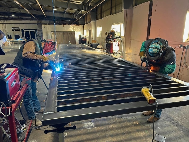 Fabricators welding a custom steel gate in a fabrication shop, showcasing the custom residential and commercial gates built in-house.