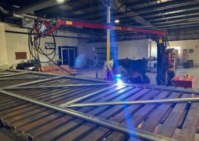 Vector Fence technician welding custom steel gate components in a fabrication shop, showcasing precision craftsmanship and professional gate construction.