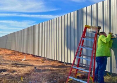 Vector Fence technician installing commercial R-panel metal fencing, demonstrating professional installation standards and durable perimeter solutions.