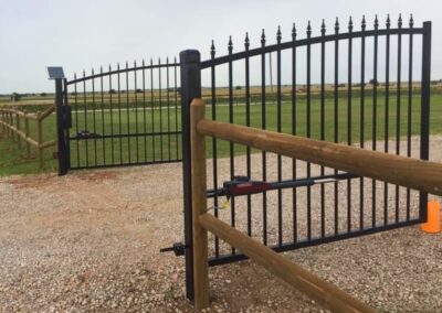 Ranch-style automatic driveway gate with ornamental steel design and solar-powered gate operator, showcasing a durable access solution for rural properties.