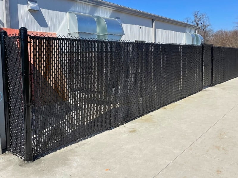 Chain Link Privacy Slats | VectorFence.com Black chain link fence with privacy slats installed beside a commercial building for added screening and security.