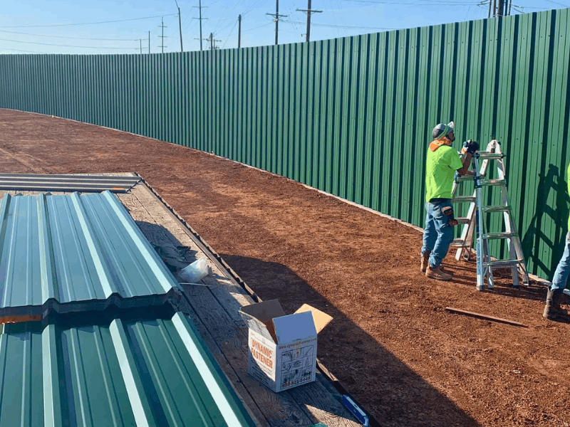 Green R-Panel Corrugated Metal Fence | VectorFence.com Green R-panel corrugated metal fence being installed along a commercial property line for privacy, security, and durability.