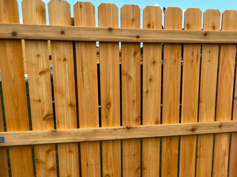 Close-up of a cedar picket fence with vertical wood boards and horizontal rails for a classic residential fence style.